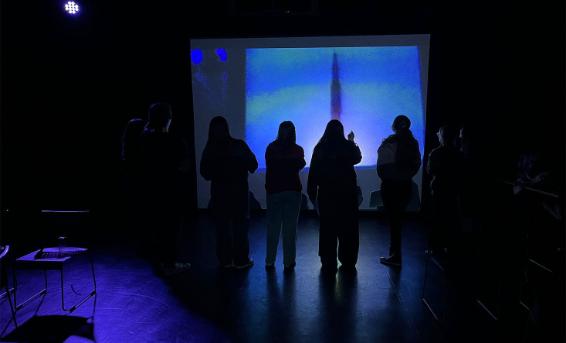 A group of Drama students rehearse in a room with a blue hue
