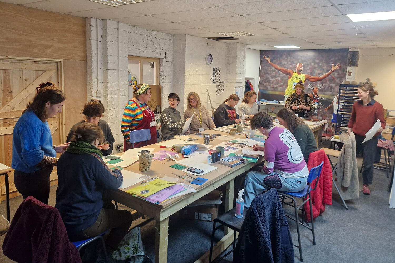 A group of people sat around a large wooden table, doing printmaking