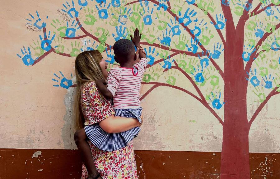 A young woman holding a child painting a handprint on a wall