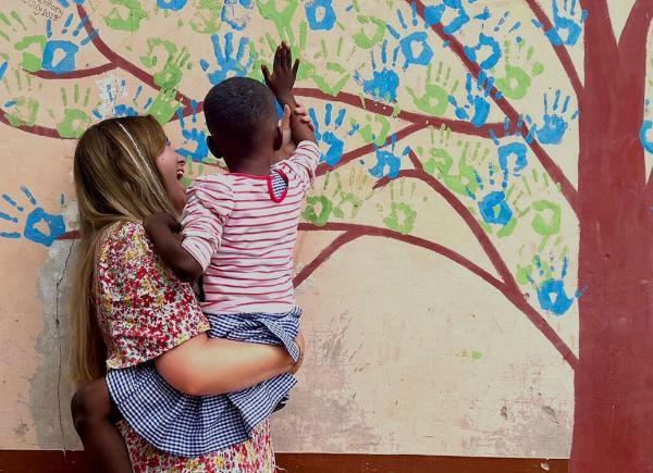 A young woman holding a child painting a handprint on a wall