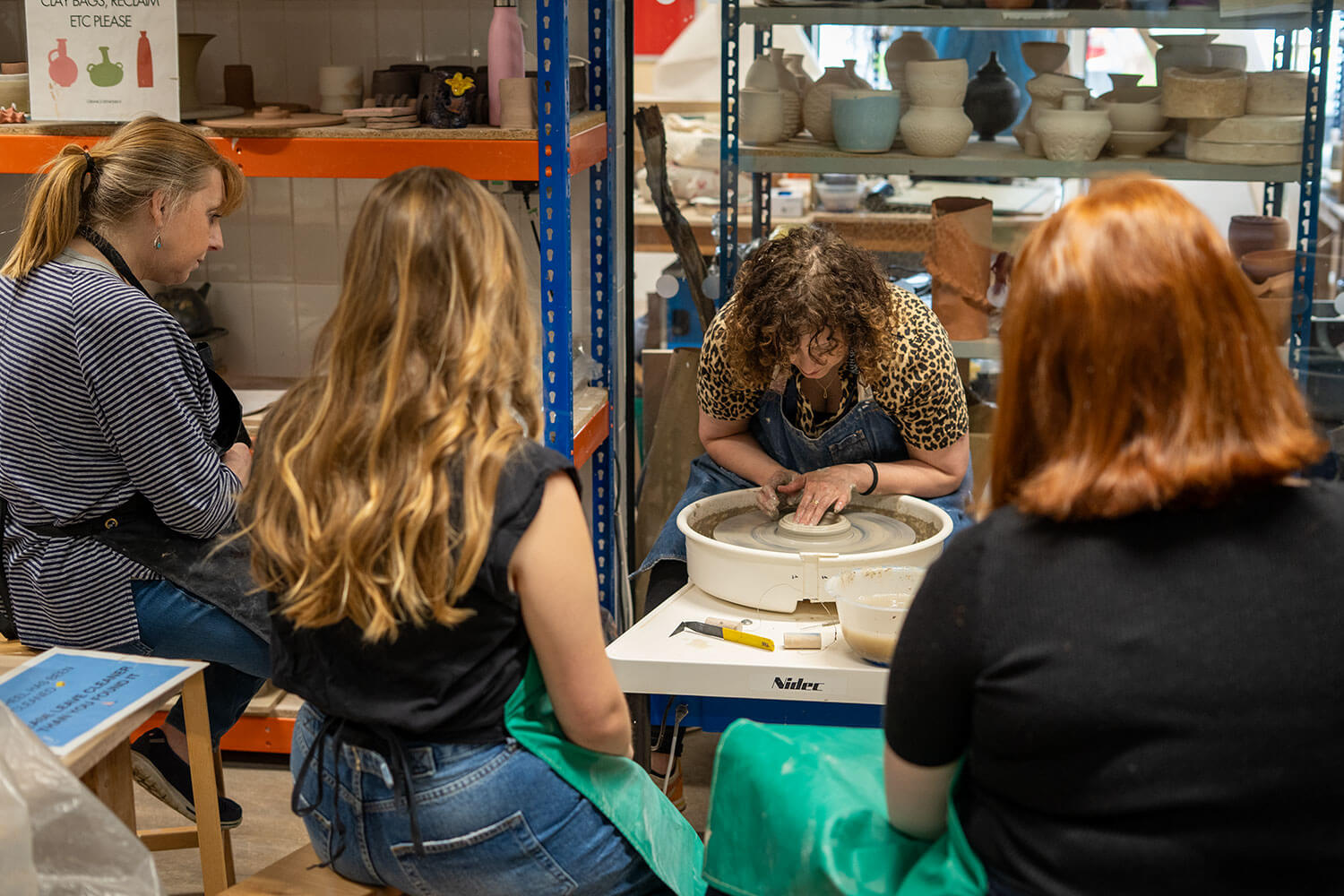 Three students watching a pottery demonstration
