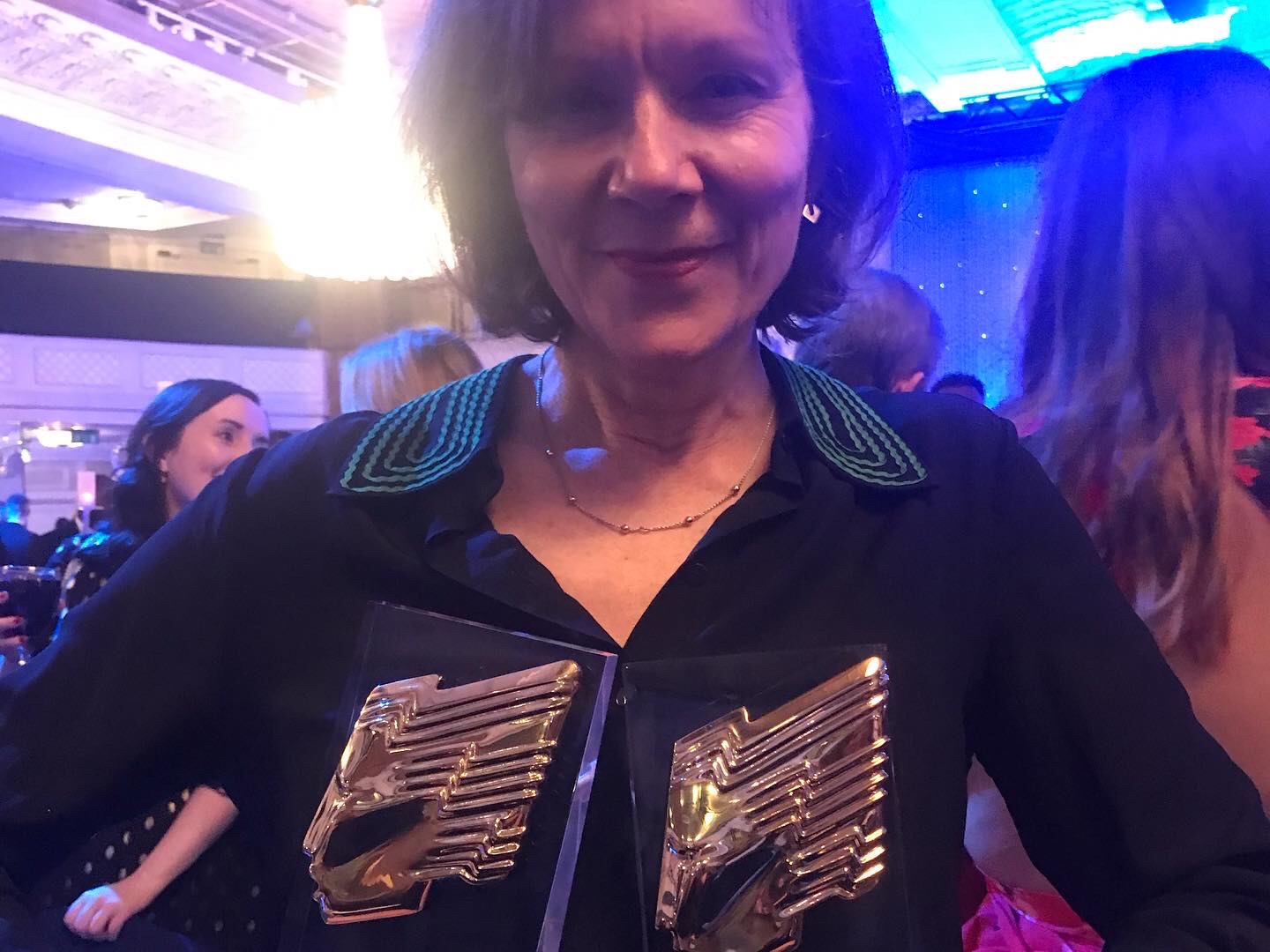 Woman in black dress holding two awards.