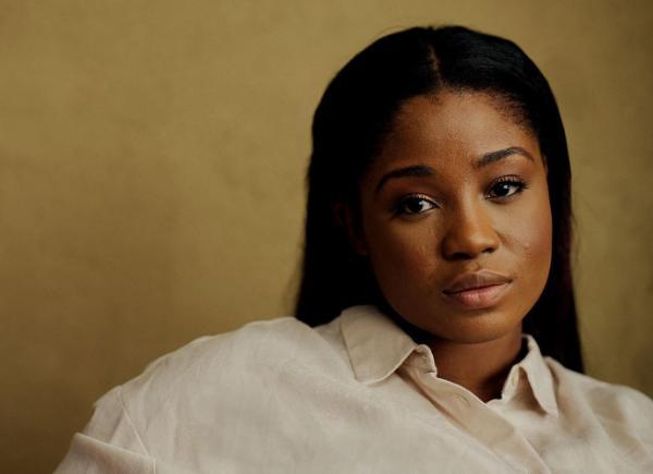 A woman sits against a yellow background in a white shirt