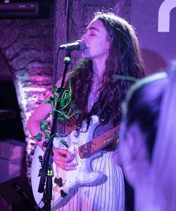 A woman with long curly hair playing a guitar and singing.