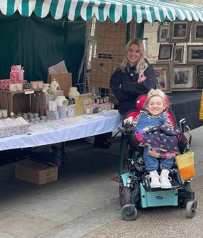 Two smiling women with blonde hair pose next to a table selling their candles.