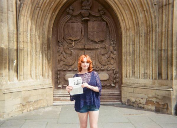 A woman stands in front of Bath Abbey, holding her dissertation