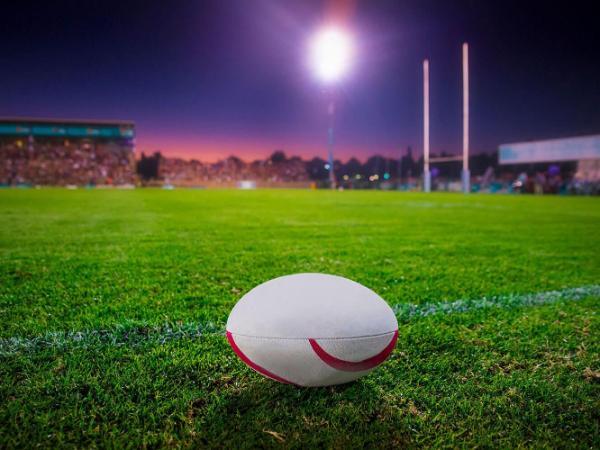 rugby ball on a grass pitch at night with flood lights in background
