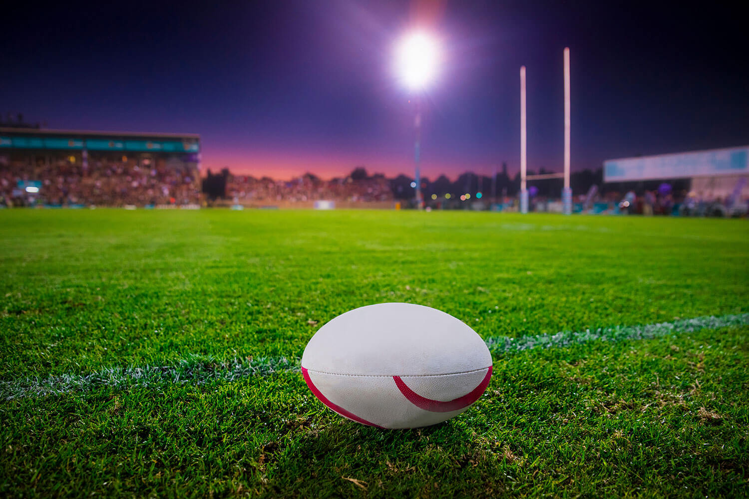 rugby ball on a grass pitch at night with flood lights in background