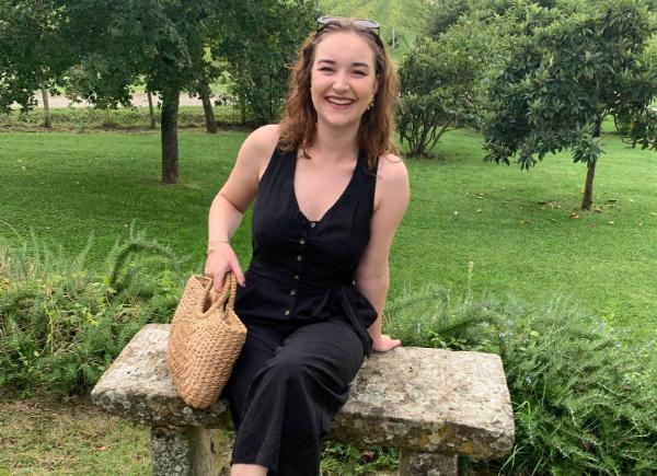 A woman sits on a bench in a black jumpsuit, smiling