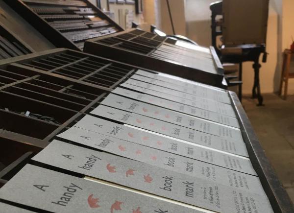 A line of printed pamphlets laid out on an old fashioned printing press.