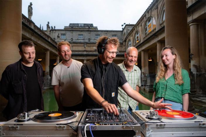 A group of people standing behind a DJ at the Roman Baths