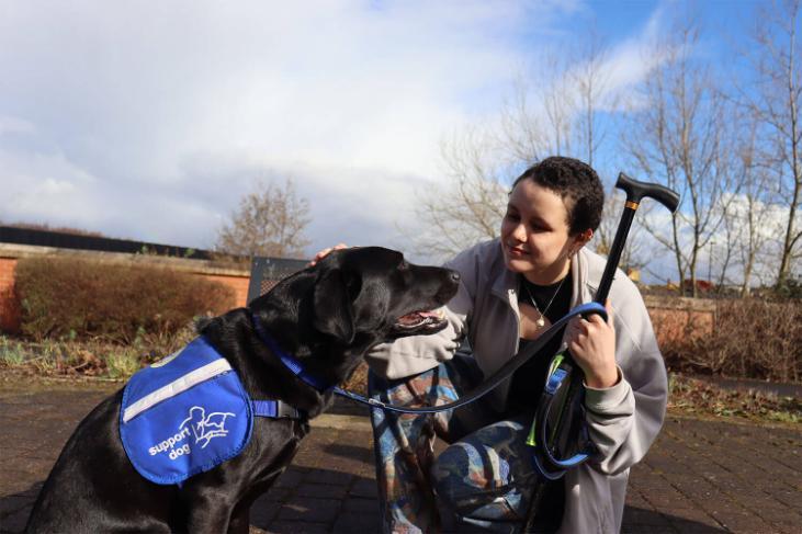 A woman with short black hair bends down to stroke a black Labrador