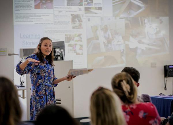 A woman gestures in front of a crowd while giving a lecture