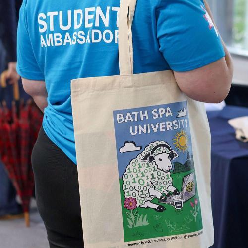A student ambassador in a blue shirt holds a tote bag with a sheep print