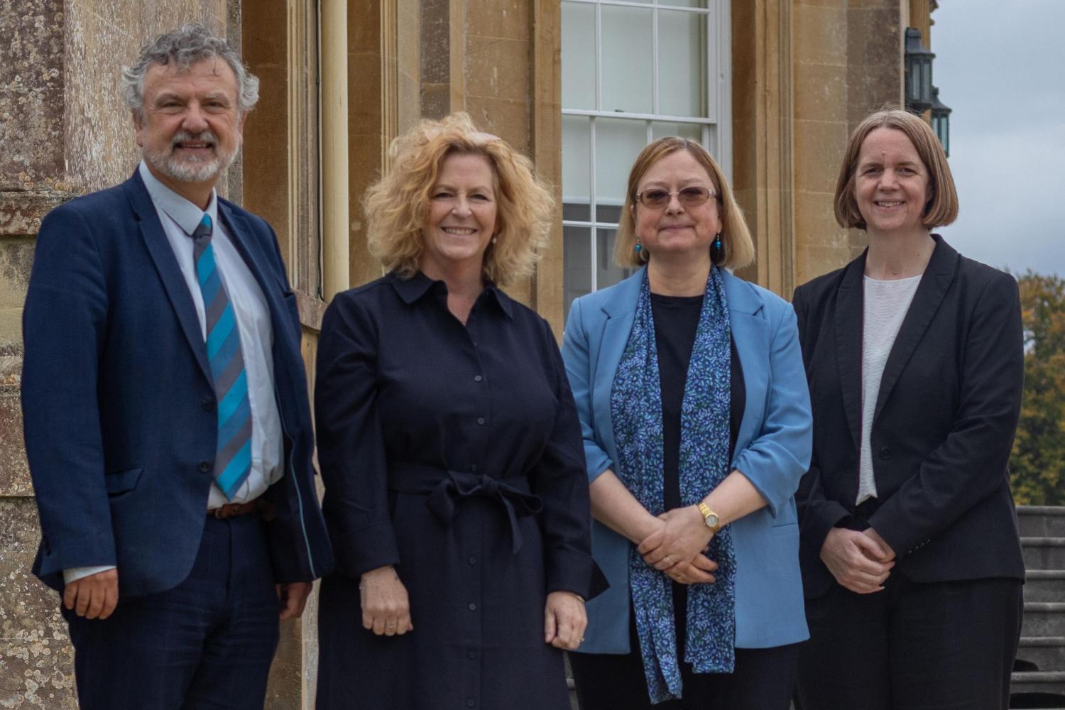 a group of people stand outside Main House at Newton Park campus, a grand building, all in smart business dress.