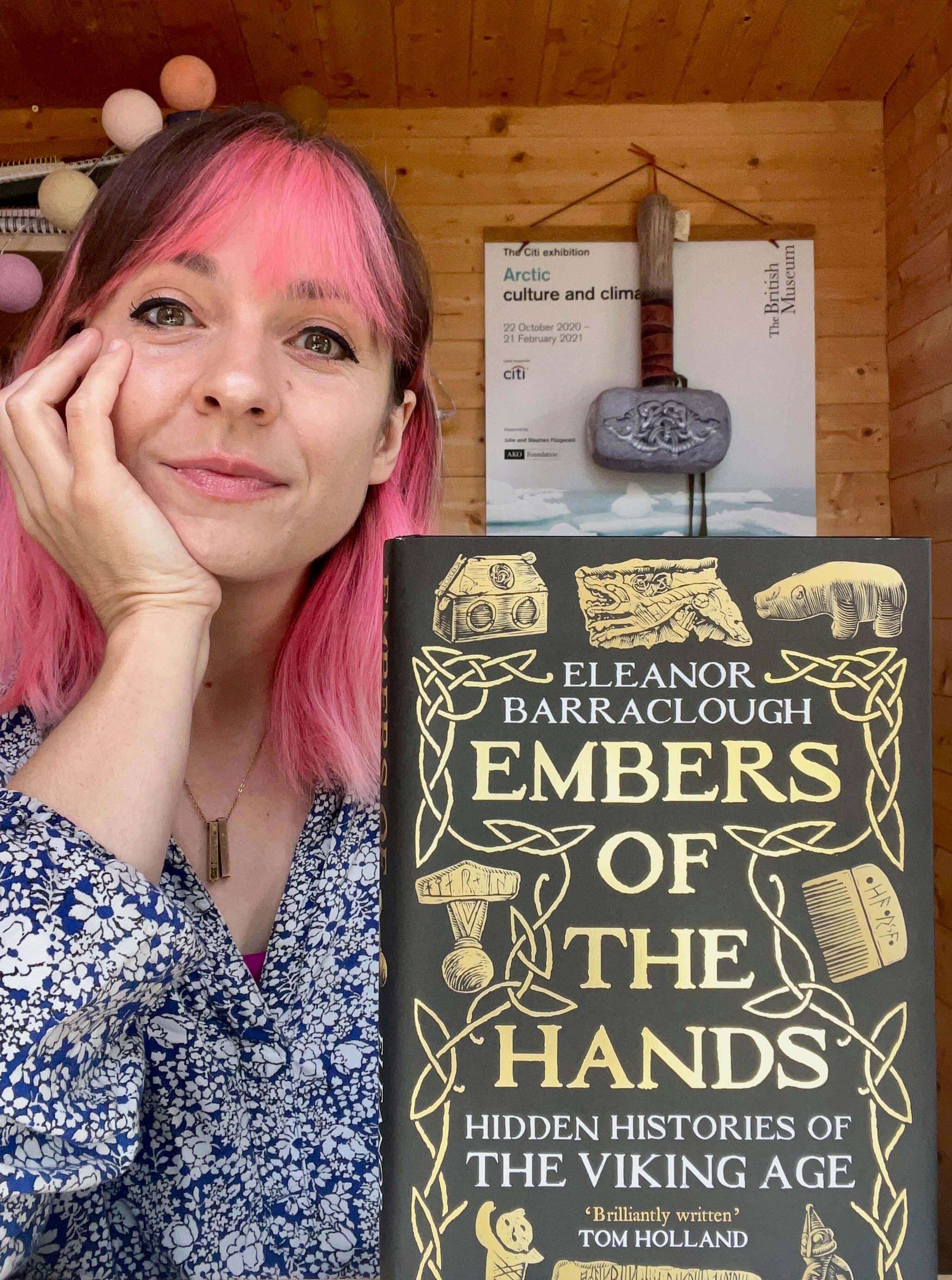 Eleanor Barraclough poses with her book Embers of the Hands. She has cool pink streaks in her hair.