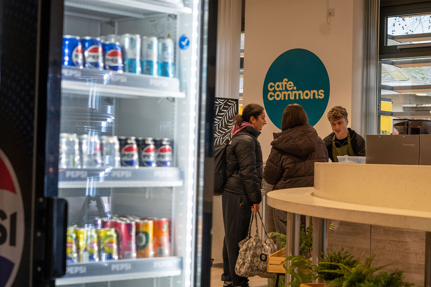 three people stood at a cafe counter, with a drinks fridge next to them