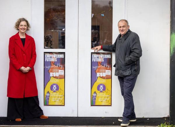 two politicians stood outside a building with posters on the door
