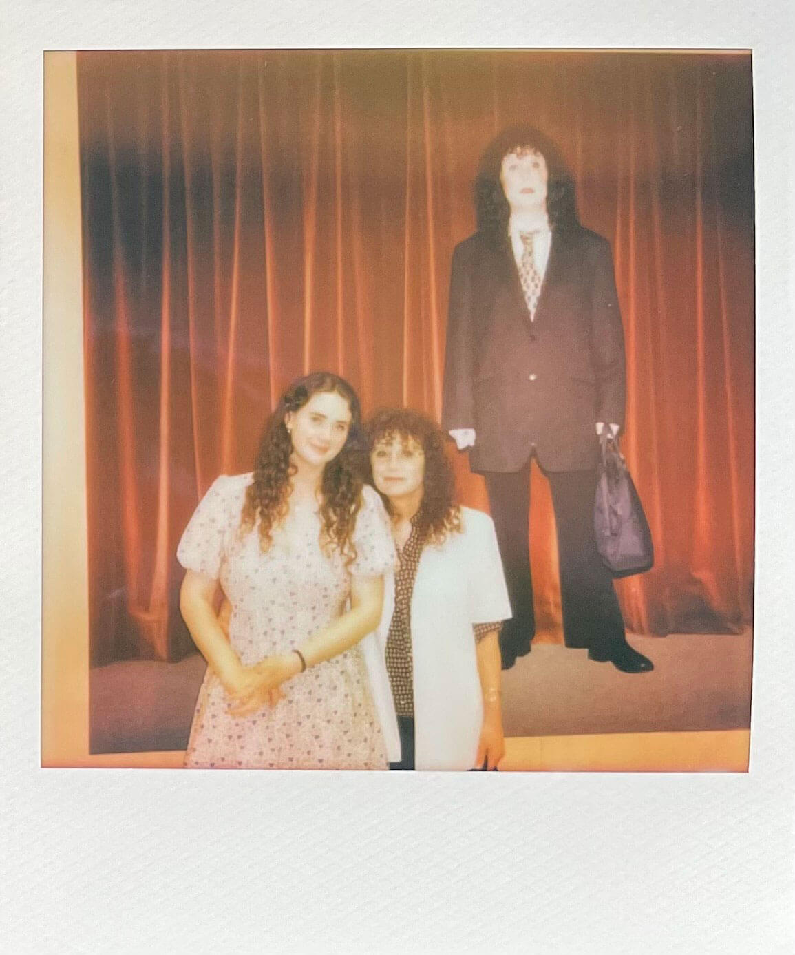 Two women stood in front of a large printout of a student artwork, depicting a woman in a suit
