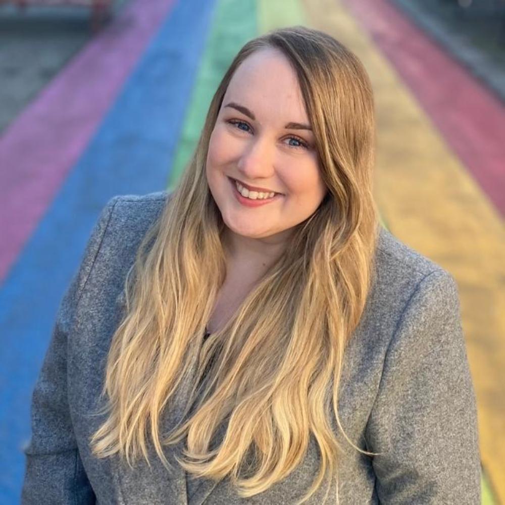 A person with long, blonde hair smiles at the camera