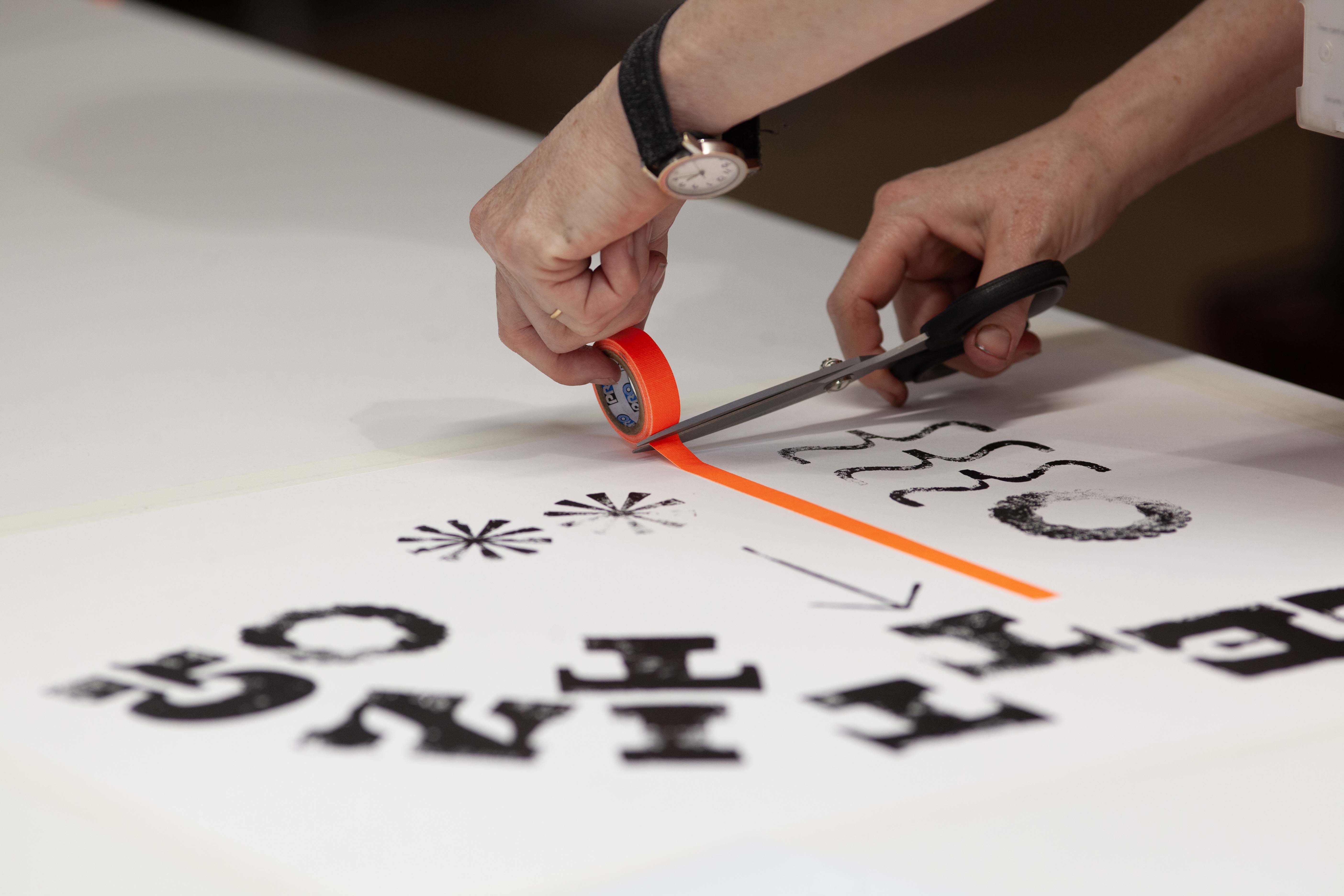 A person cutting brightly coloured orange tape with scissors