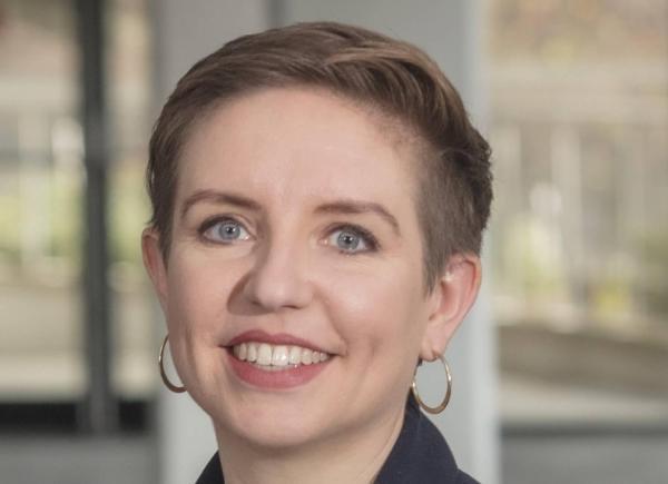 A person with short, cropped hair and hoop earrings smiles at the camera