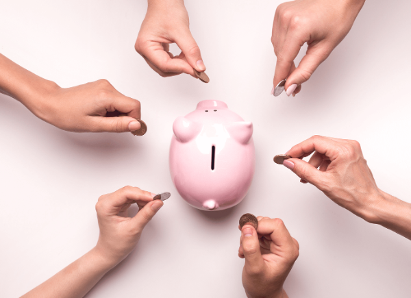 Six hands hold a coin each and move towards a pink pig shaped money bank.