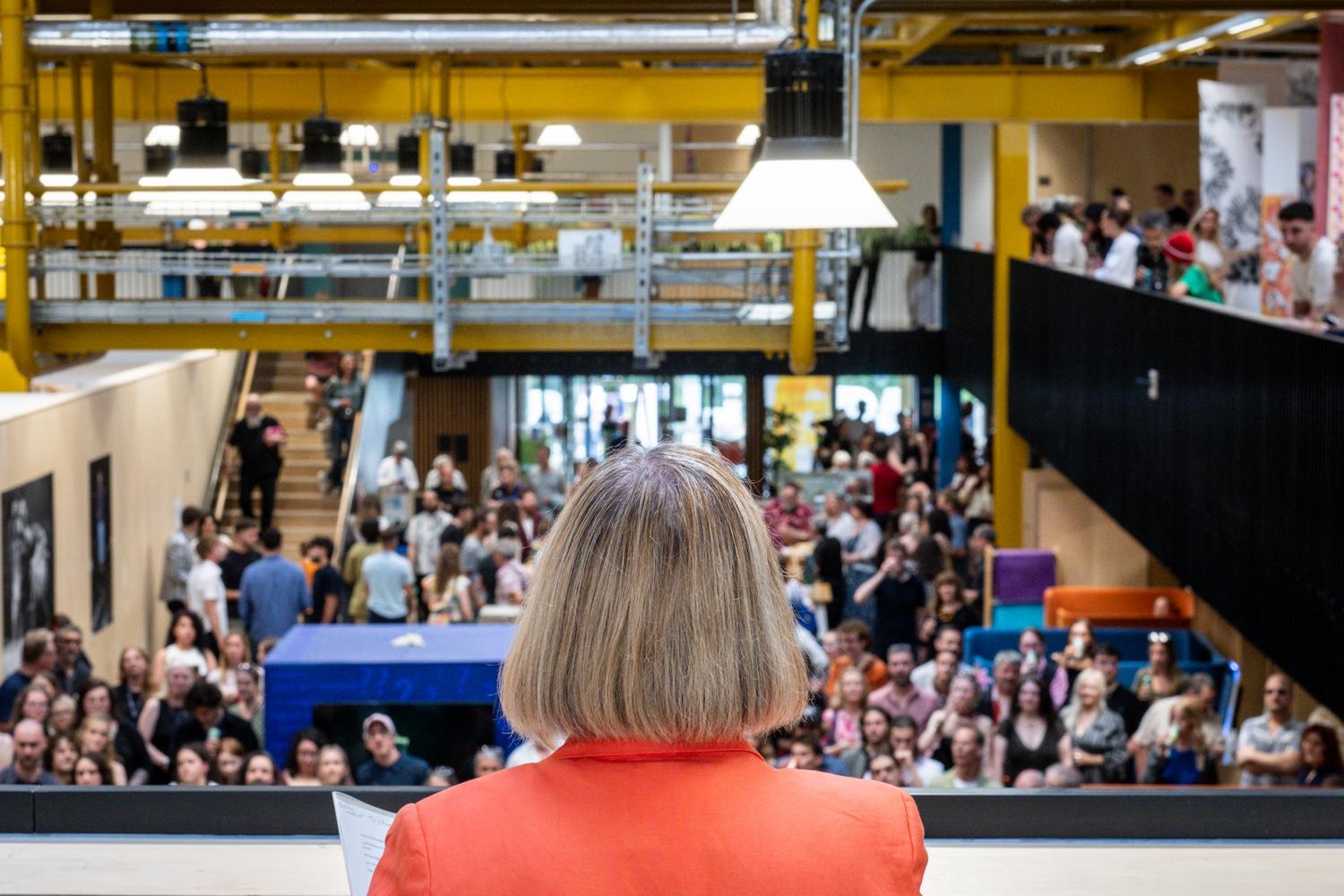 A wide shot of a crowd of people looking up at the speaker in the foreground