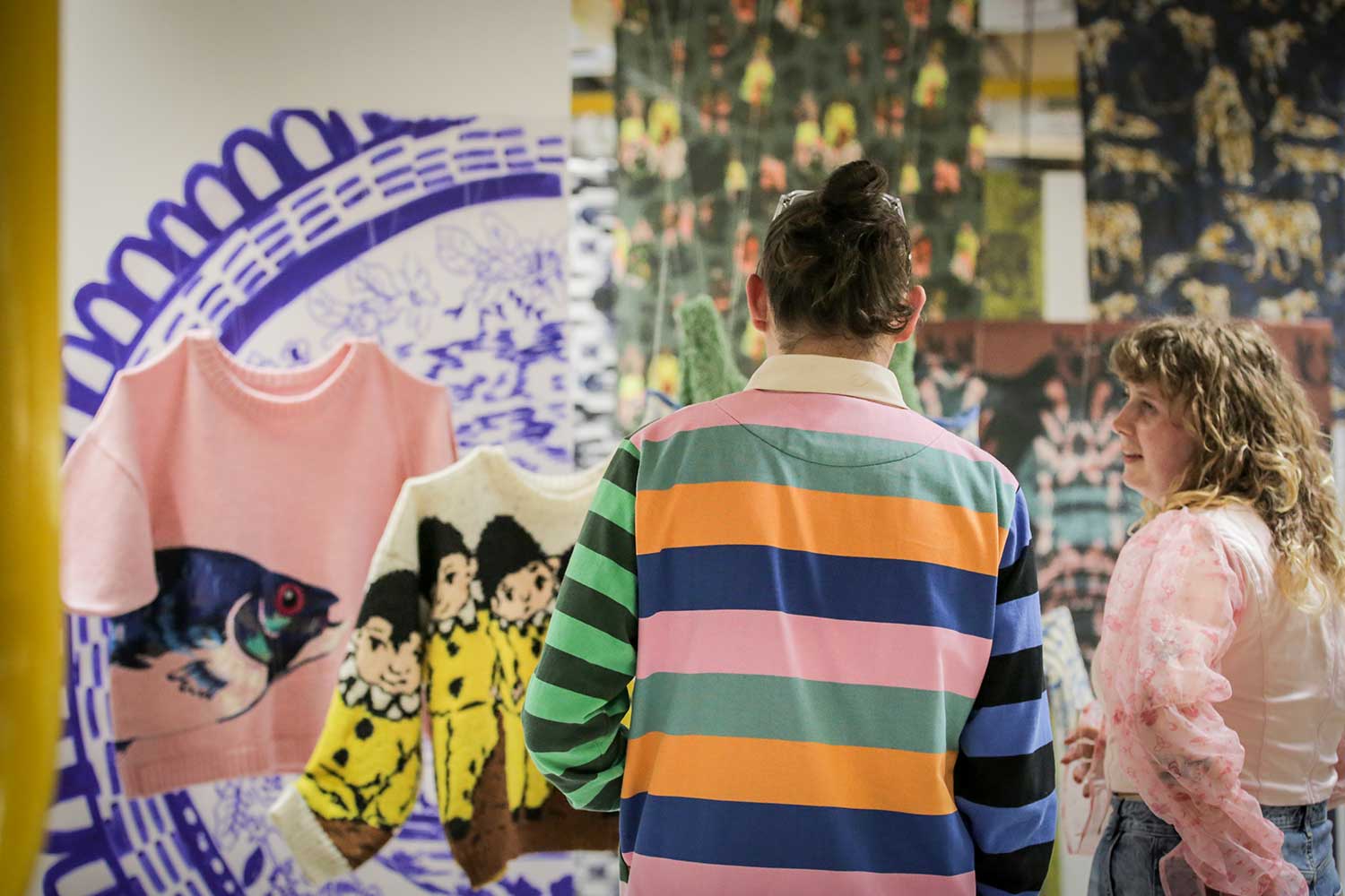 Two people view a display of colourful knitted sweaters