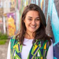 Photo of person with long dark hair and colourful jacket leaning against a wall