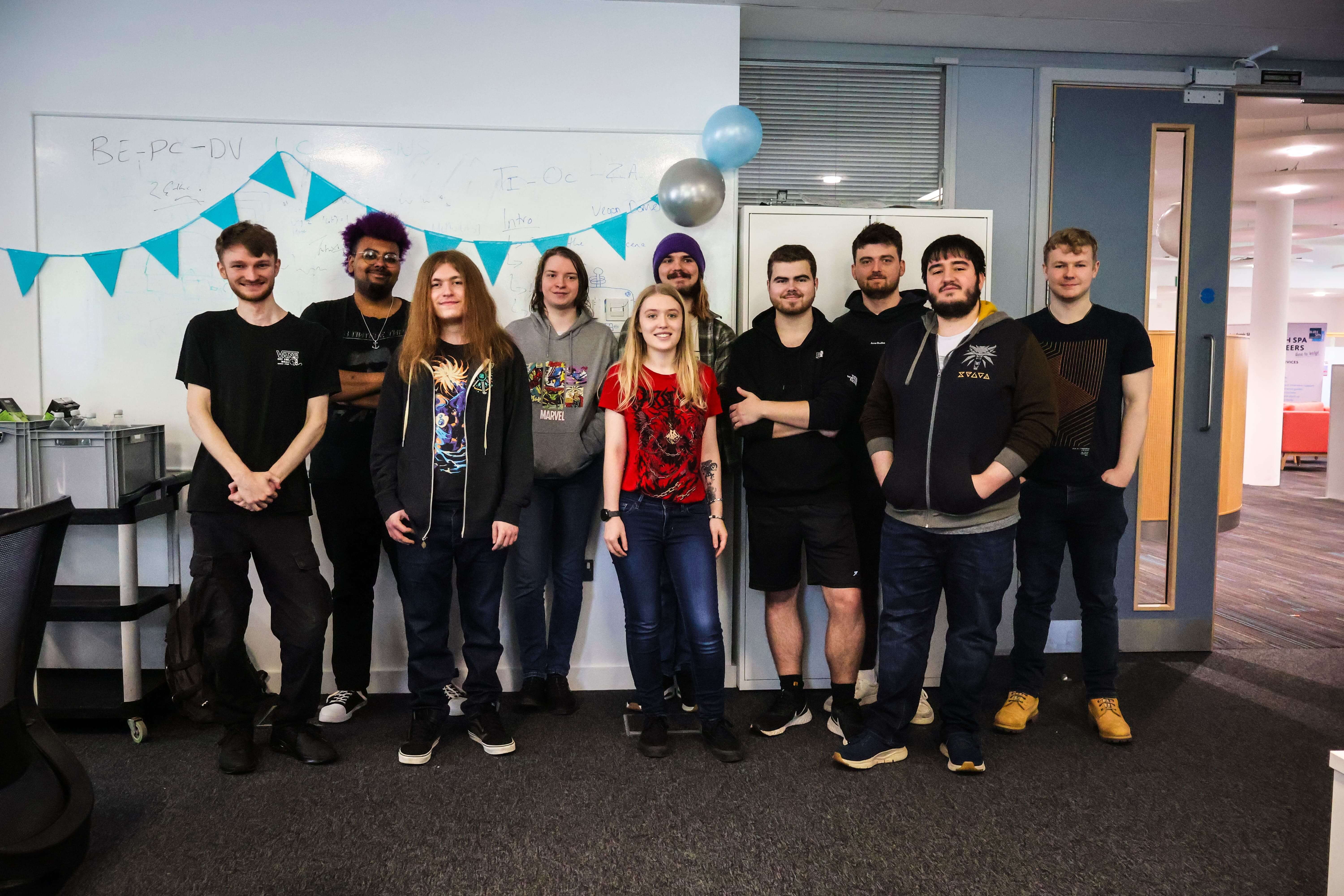 A group of students posing for a photo, stood in front of a whiteboard