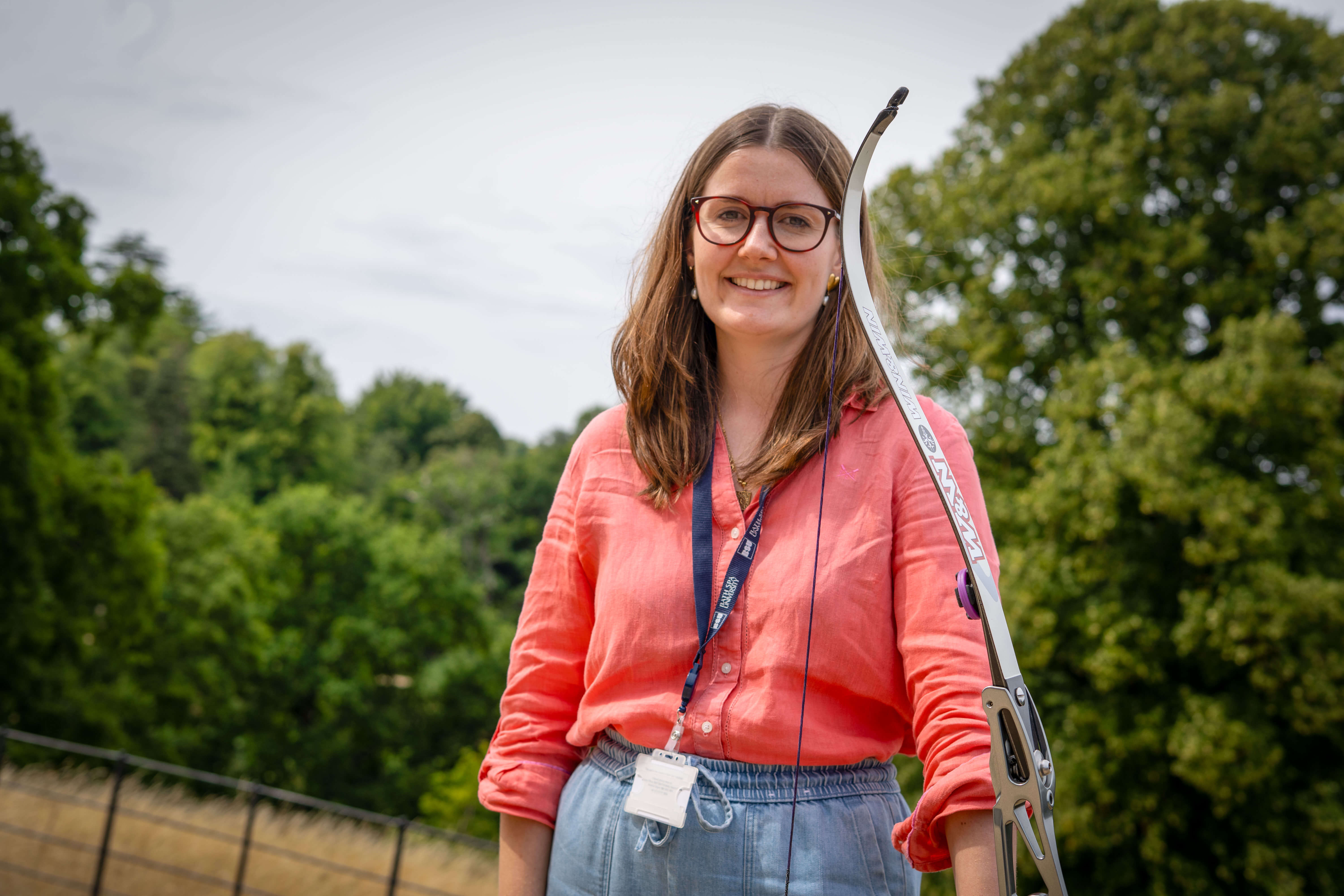 A woman holding a bow and arrow smiling at the camera