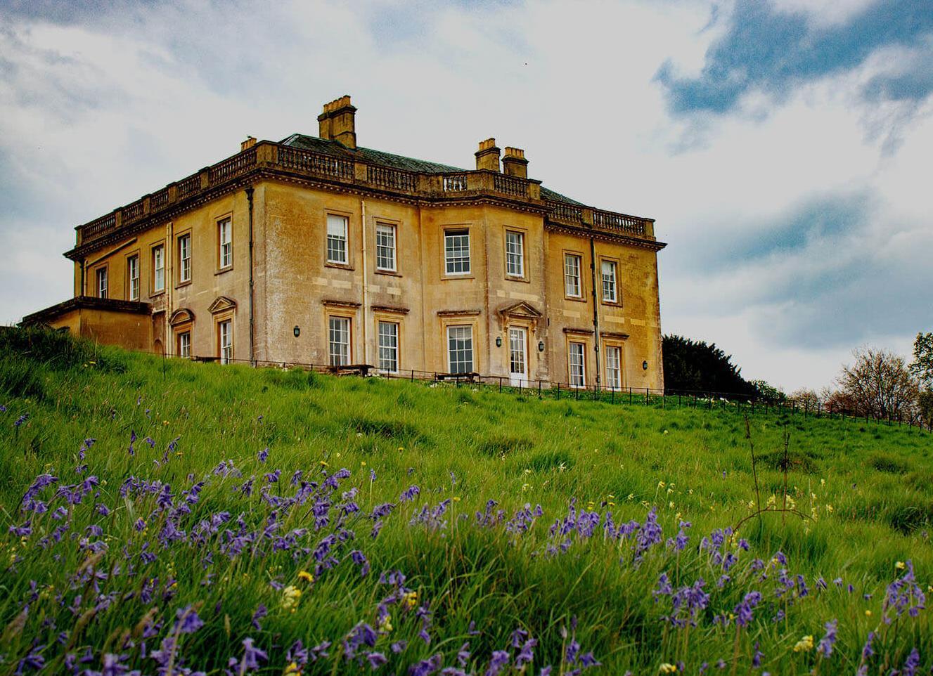 A mansion house on the horizon with grass and bluebells in the foreground