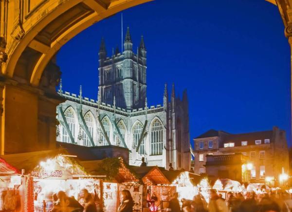 Bath Abbey at dusk surrounded by wooden Christmas Market huts