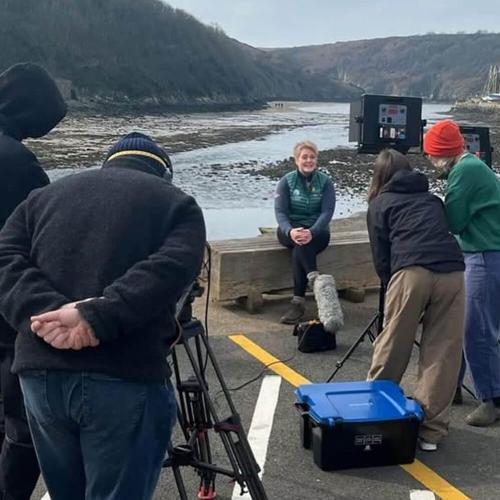 a film crew interviewing a lady sat in front of a beach