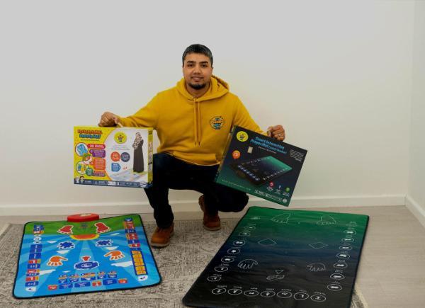 Kamal Ali crouches down behind the two interactive prayer mats he has created, holding the boxes for each