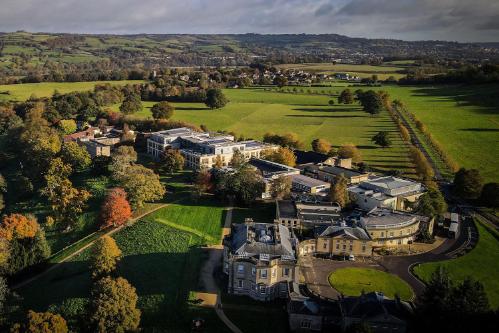 A drone shot of Newton Park in the autumn, featuring large buildings, green fields and orange trees