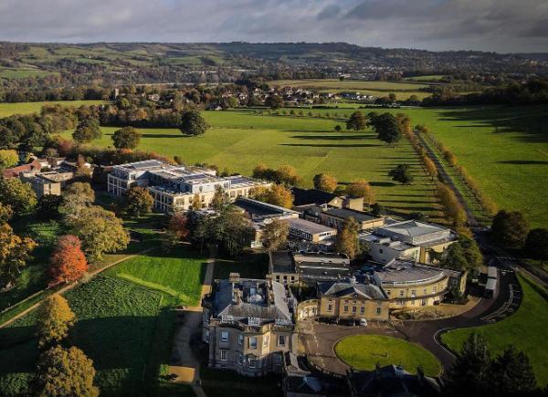 A drone shot of Newton Park in the autumn, featuring large buildings, green fields and orange trees