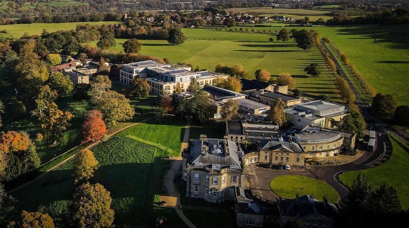 A drone shot of Newton Park in the autumn, featuring large buildings, green fields and orange trees