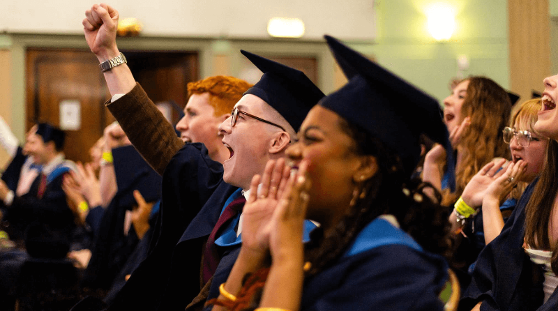 Two rows of students at their final year graduation looking at the stage and cheering. 