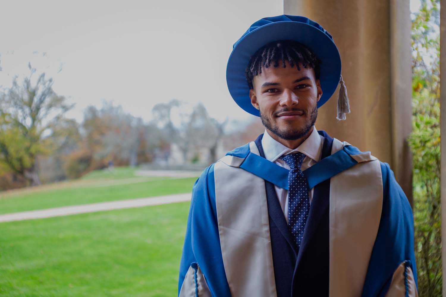 Tyrone Mings smiling at camera wearing graduation robes in the grounds of Newton Park campus