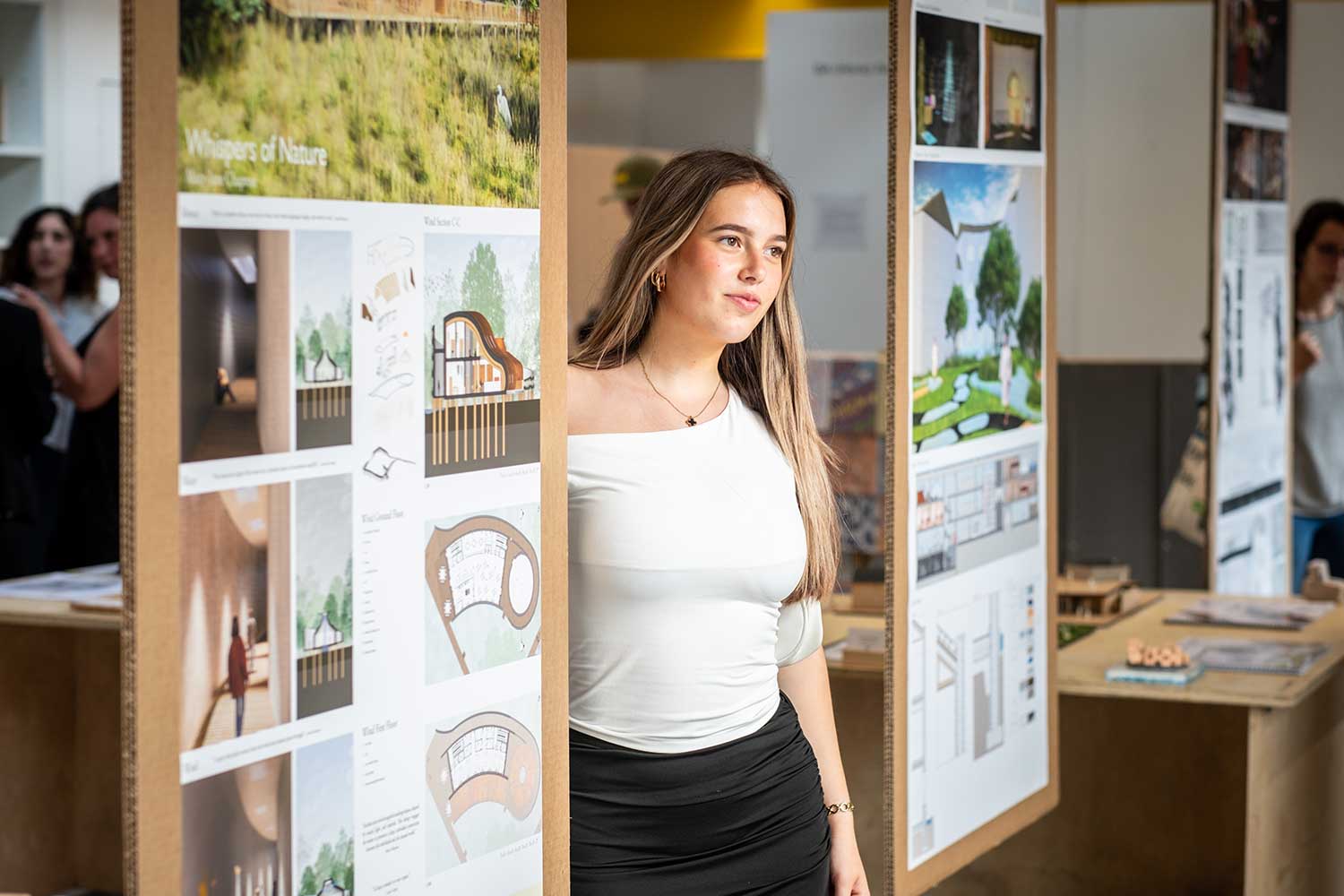 A student stands in front of a display board full of her work