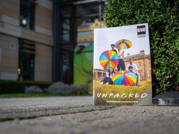 Unpacked magazine leant up against a hedge outside Commons