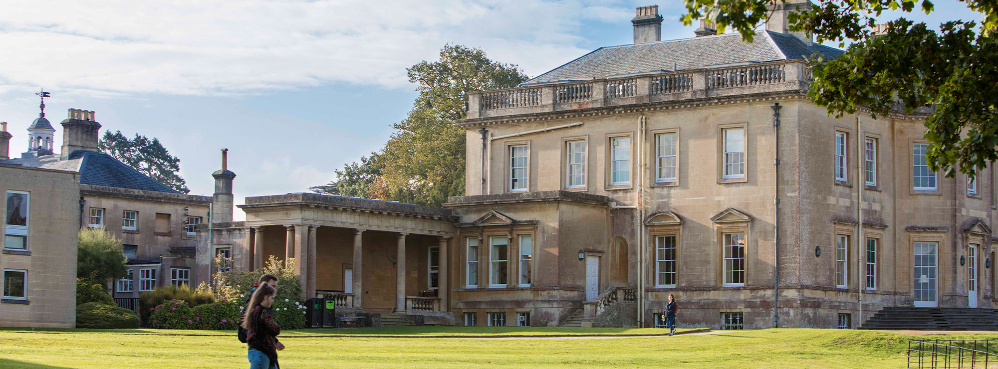 Two students walking in front of the Main House at Newton Park campus.