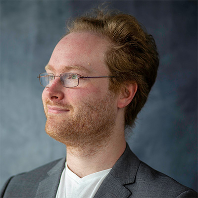 Headshot of someone with short hair and glasses in white top and jacket