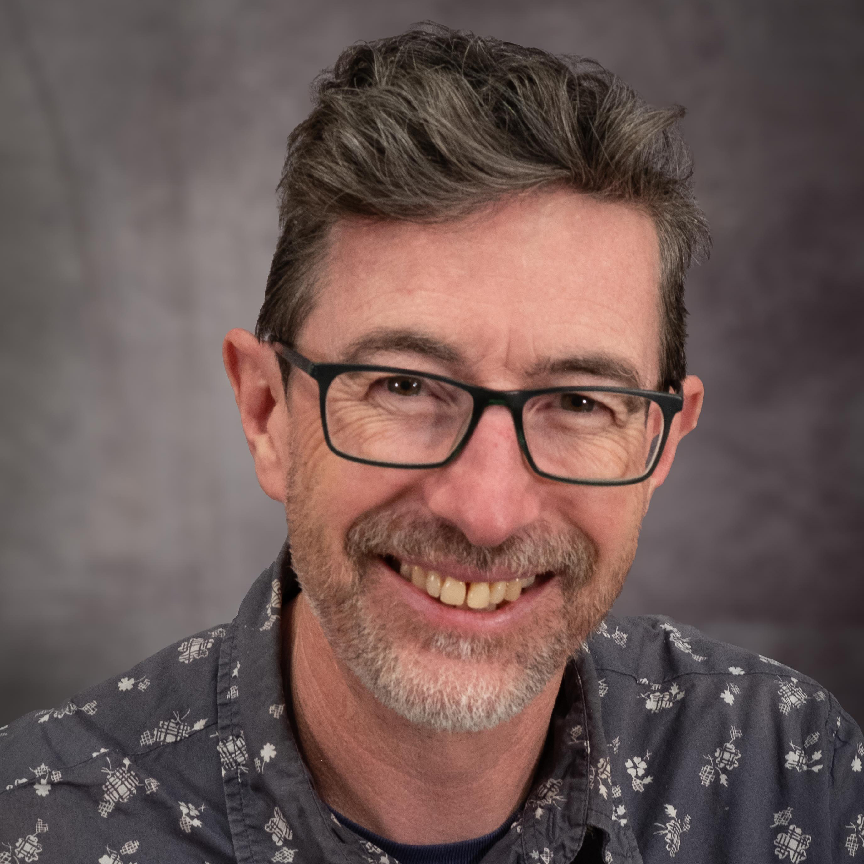 A smiling staff member of Bath Spa University stands against a mottled grey backdrop.
