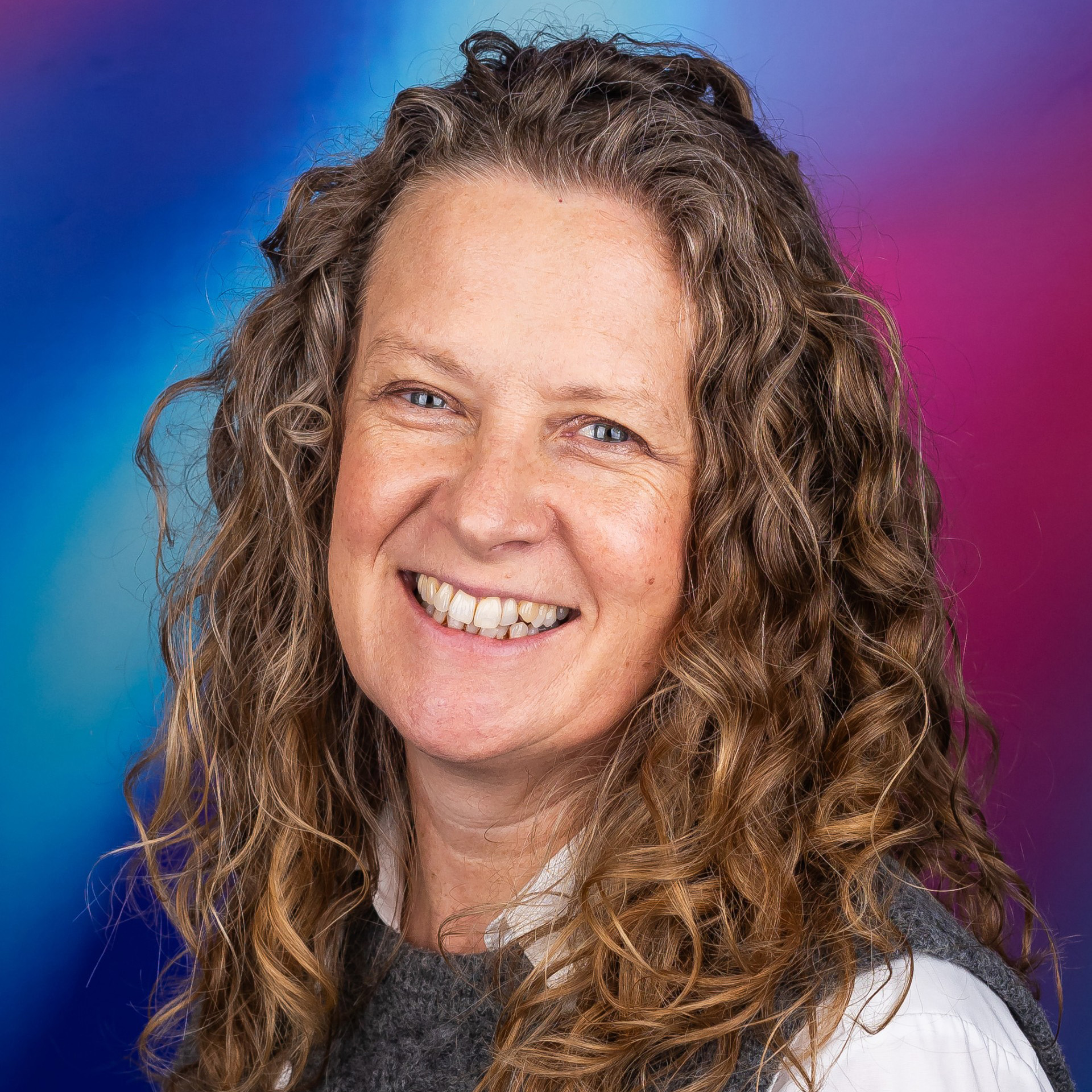 A Bath Spa University staff member is pictured smiling against a bright blue and purple background.