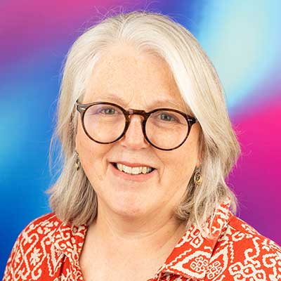 A person with pale grey hair and dark glasses smiles at the camera