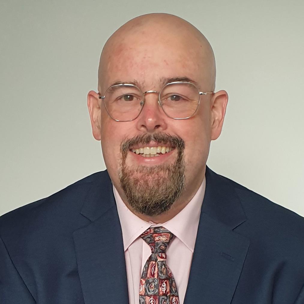 Profile picture of a man in glasses and a suit and tie against a white background.
