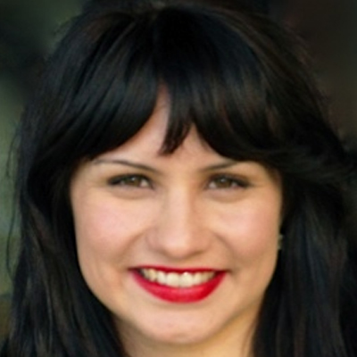 Headshot of someone with long dark hair with fringe smiling. They are wearing crimson lipstick